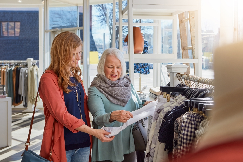 UK female couple shopping in small fashion outlet store.